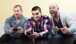 Three positive adult guys sitting on sofa with joysticks indoors