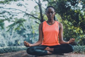 Woman in yoga clothes meditating to battle addiction in park.
