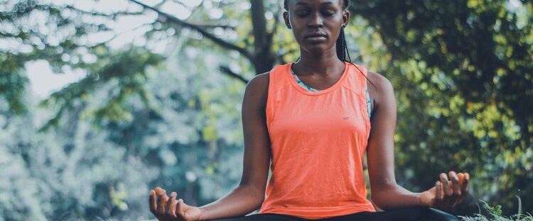 Woman in yoga clothes meditating to battle addiction in park.