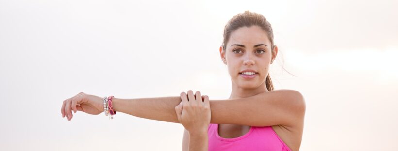 Woman in pink exercise gear stretching her arm.
