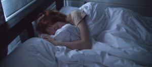 Woman with red hair sleeping in bed with white sheets.