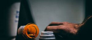 Dark photo of drugs on table with mans hand tensely gripping, close to relapse.