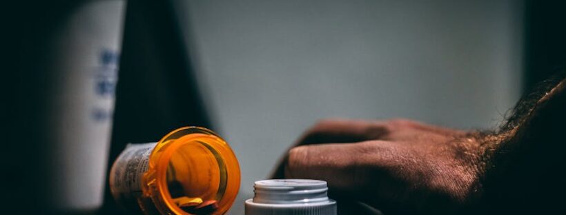 Dark photo of drugs on table with mans hand tensely gripping, close to relapse.
